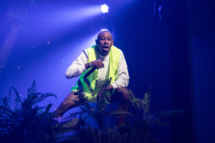 Tyler, the Creator performing a song infront of a crowd in his neon green sash