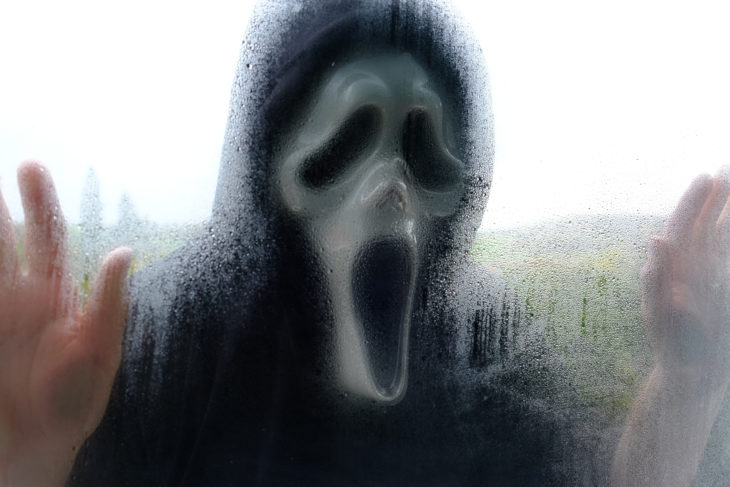 Halloween holiday. scream mask.A man in a ghost costume in a muddy blurry window.halloween fashion festival concept.white ghost mask cosplay.Autumn holidays