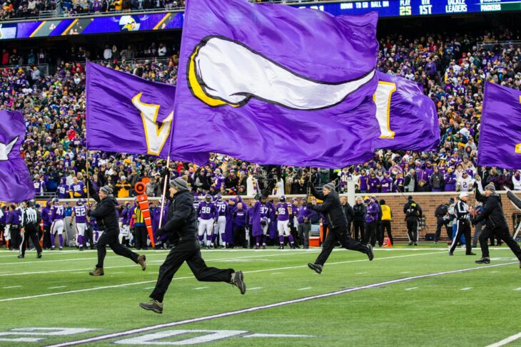 people running and holding Minnesota Vikings flags in green field